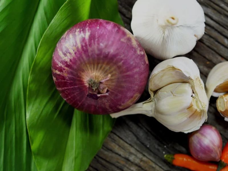 prikaz belog i crvenog luka na drvenom stolu sa listom salate i papričicama